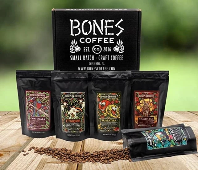 Five four ounce bags of coffee are in front of a box. The box has the Bones Coffee Company logo on it. The bags of coffee are named Guatemala, Ethiopia, Sumatra, Colombia, and Costa Rica.